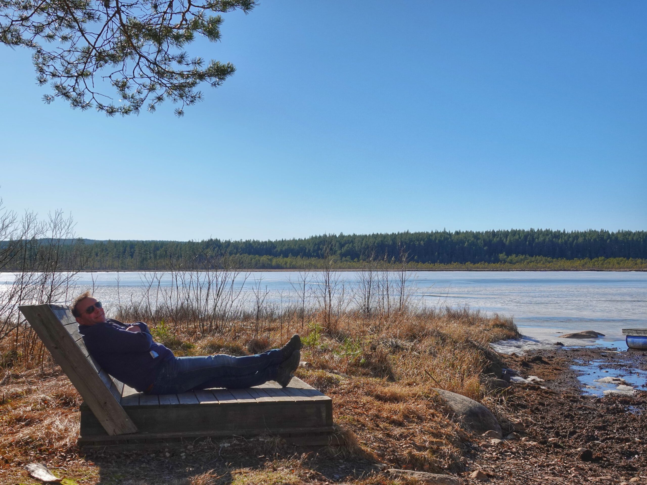 Erik ontspant op een houten ligbank aan het meer na een wandeling door Värmland