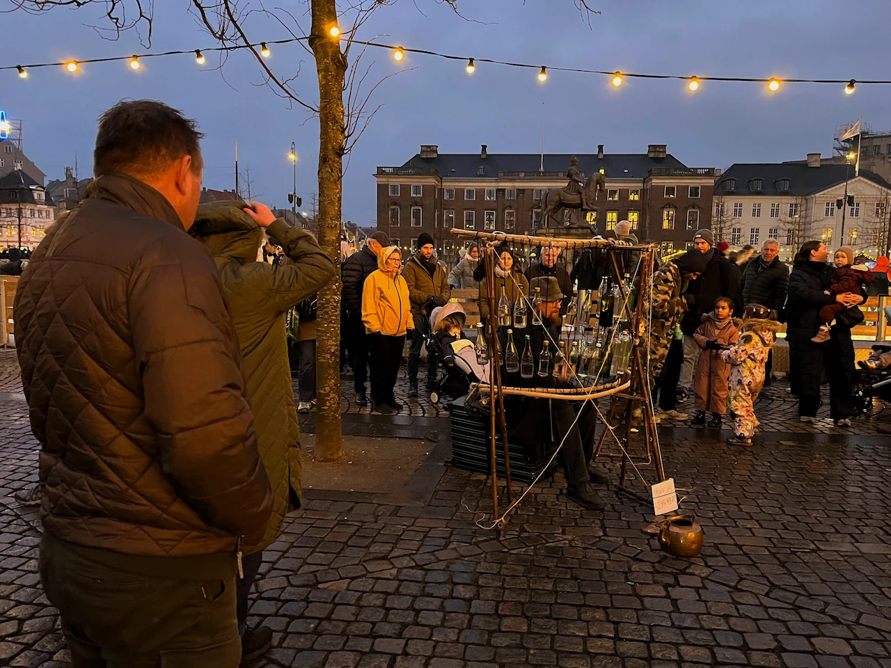 Erik kijkt naar een straatmuzikant in Kopenhagen die muziek maakt op een zelfgemaakt instrument van lege flessen.