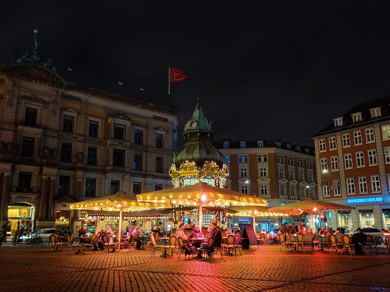 Gezellige sfeer bij Espresso House op Kongens Nytorv met verlichte parasols en mensen onder dekentjes.