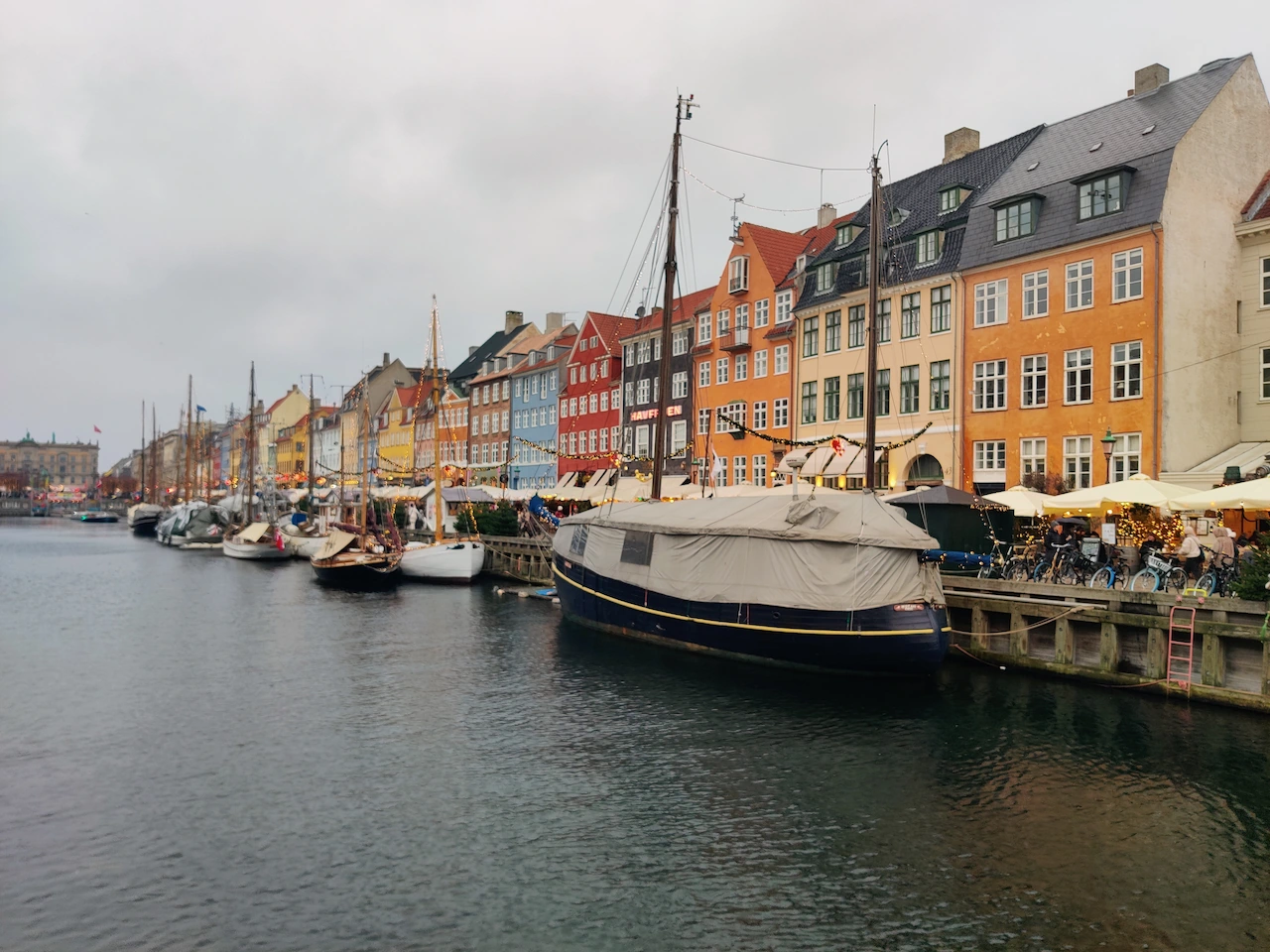 Uitzicht over het water op de verlichte kerstkraampjes en gekleurde gevels van Nyhavn in kerstsfeer met boten.