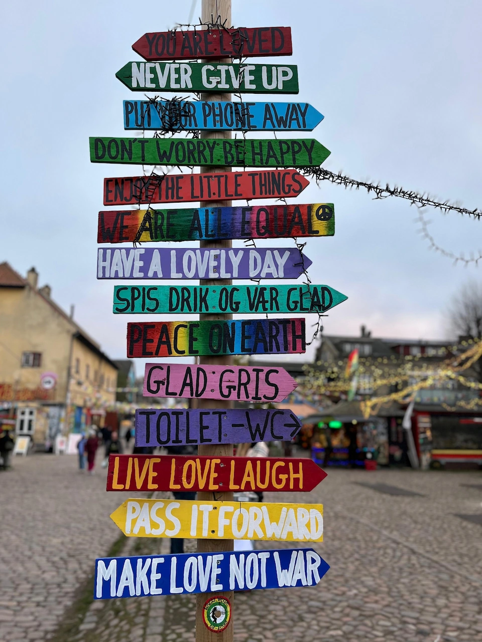 Een kleurrijk houten wegwijzerbord in Christiania met inspirerende teksten op pijlen zoals 'Make love not war' en 'Never give up'