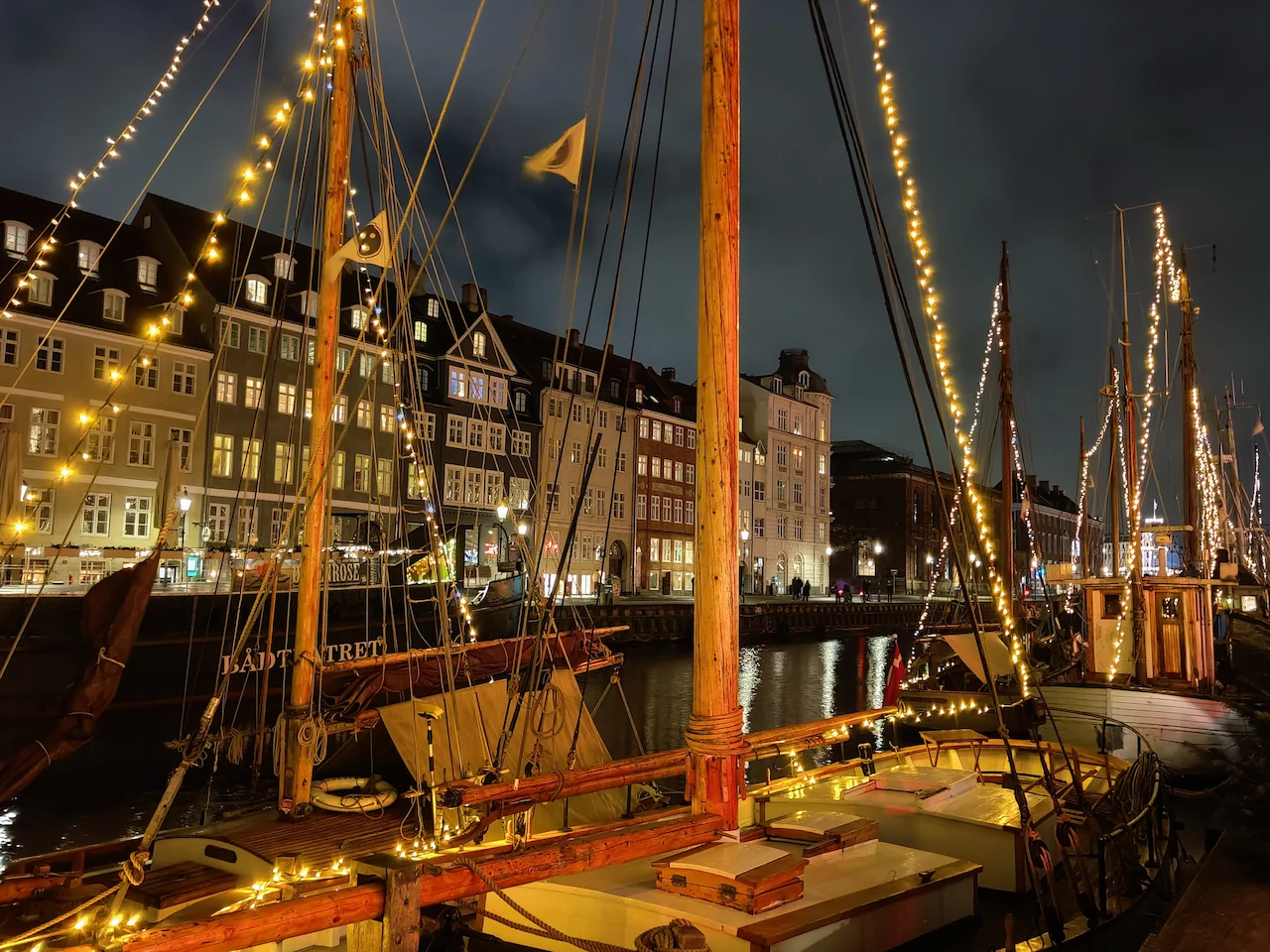 Verlichte boten in de haven van Nyhavn Kopenhagen met de iconische gekleurde gevels op de achtergrond bij avond.