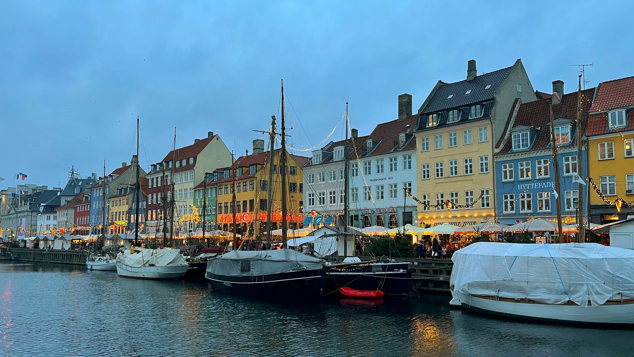 Sfeervol verlichte gevels van Nyhavn in Kopenhagen met historische boten en gezellige kraampjes langs de kade bij avond.