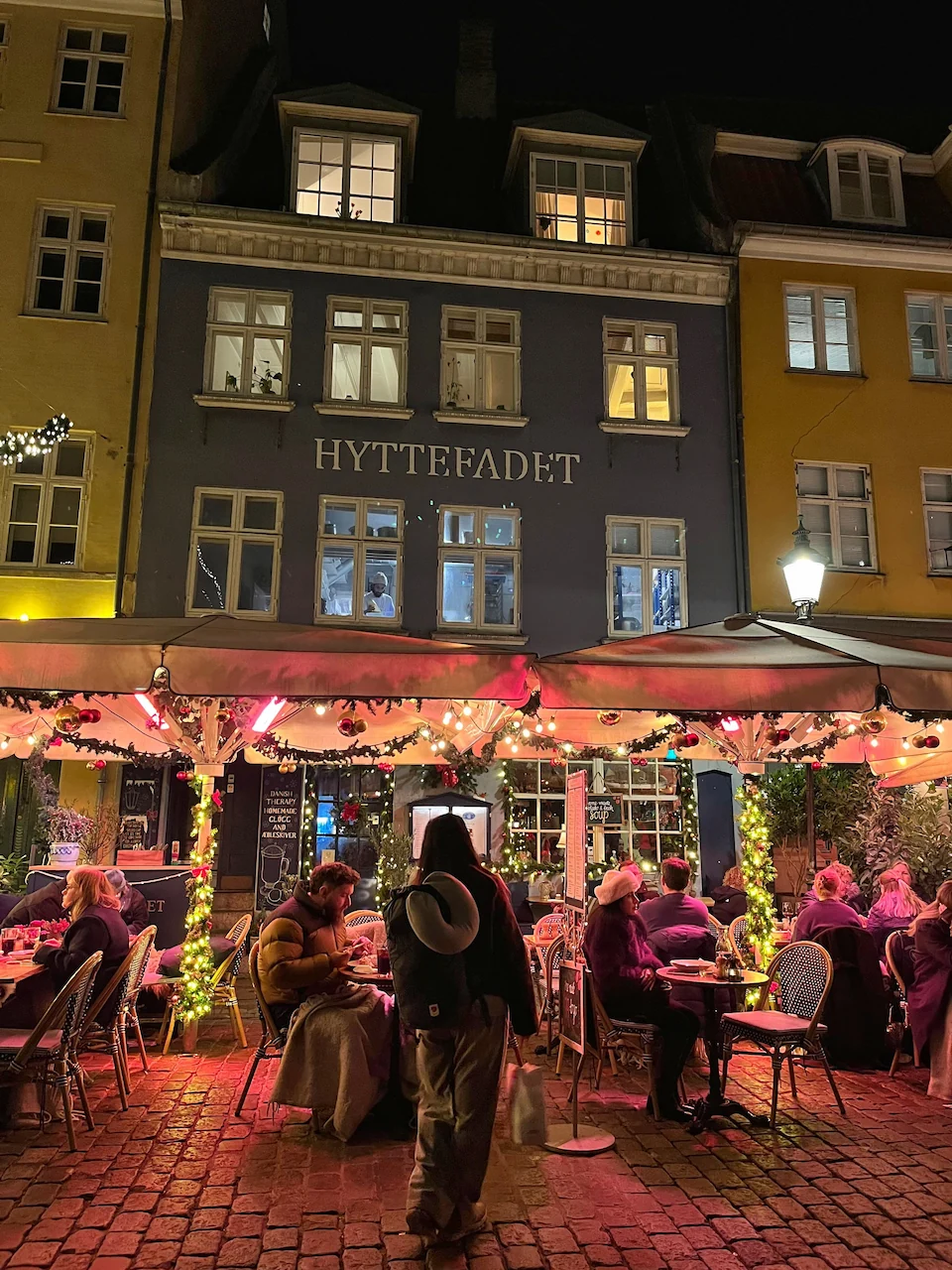 Gezellig druk terras van restaurant Hyttefadet in Nyhavn bij avond met sfeervolle verlichte parasols.