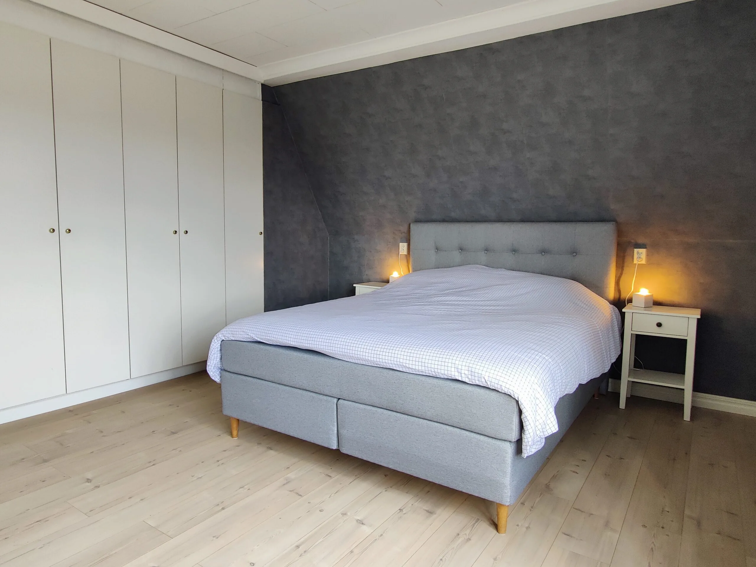 Sfeervolle slaapkamer met grijs behang, tweepersoons boxspring en grote kastenwand