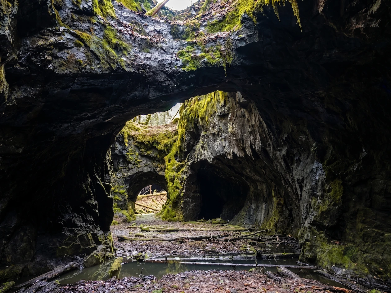Blik van binnenuit de historische mijn Tilas stoll met indrukwekkende rotswanden, groen mos en openingen naar de buitenlucht.